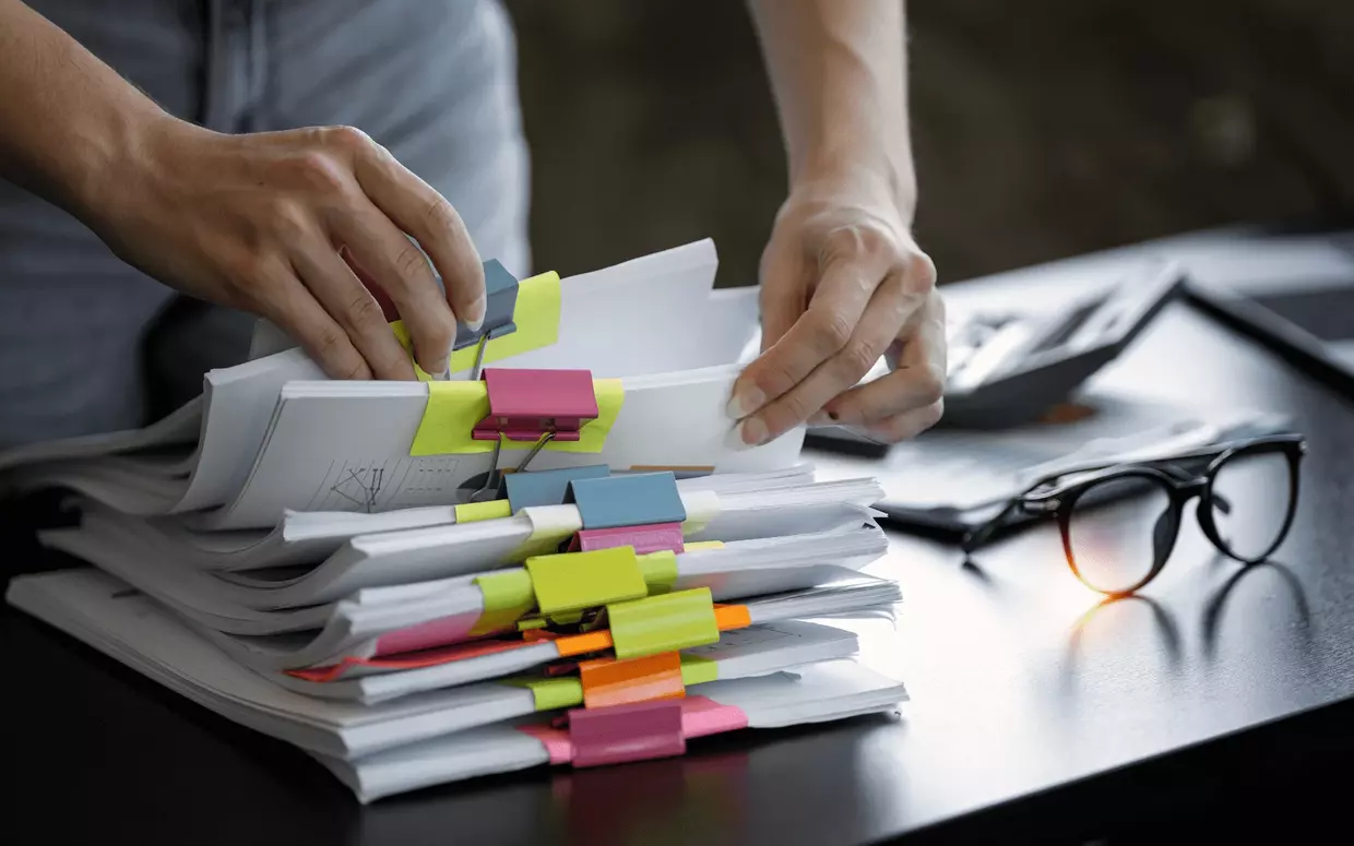 Person am Schreibtisch sucht gezielt in geklemmtem Papierordnern.