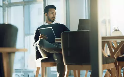 Ein Mann mit verschränkten beinen vor einem Laptop.