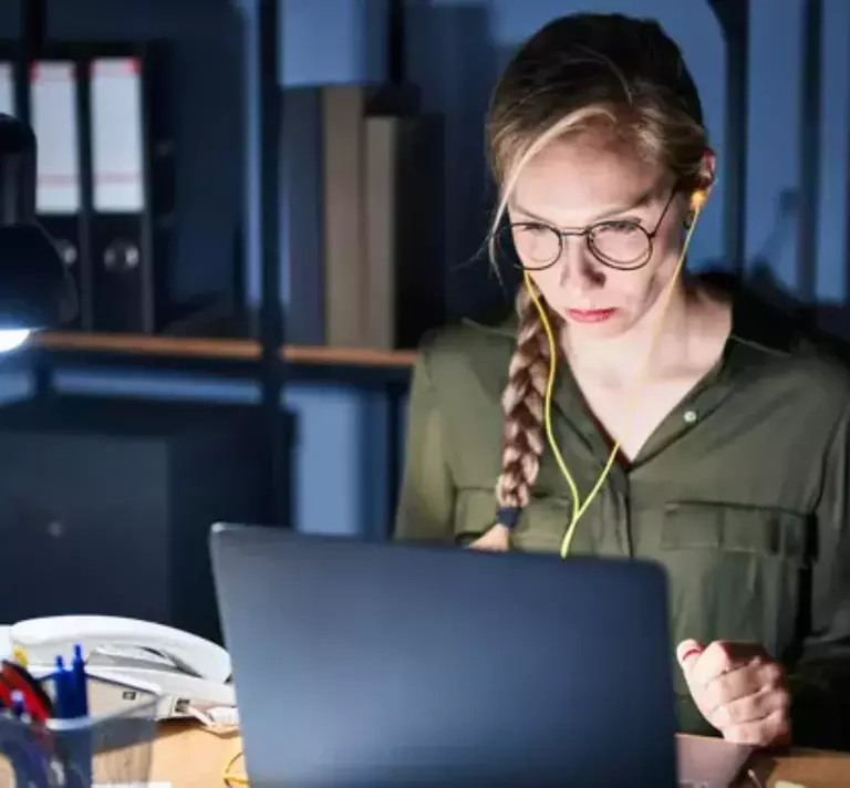Zahlungsverzug dargestellt durch konzentrierte Frau mit Brille und Kopfhörern, die nachts an beleuchtetem Schreibtisch arbeitet.