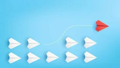 Wachstum dargestellt durch roten Papierflieger, der aus Formation weißer Flieger ausschert und nach oben fliegt.