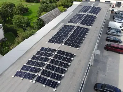 Eine Luftaufnahme von einem Gelände mit Grünflächen und Gebäuden mit Photovoltaikanlage auf dem Dach.