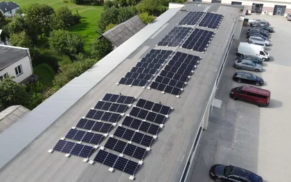 Eine Luftaufnahme von einem Gelände mit Grünflächen und Gebäuden mit Photovoltaikanlage auf dem Dach.