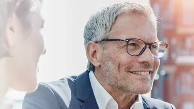 Wachstum symbolisiert durch lächelnden älteren Geschäftsmann mit Brille im Gespräch mit Kollegin in hellem Büro.