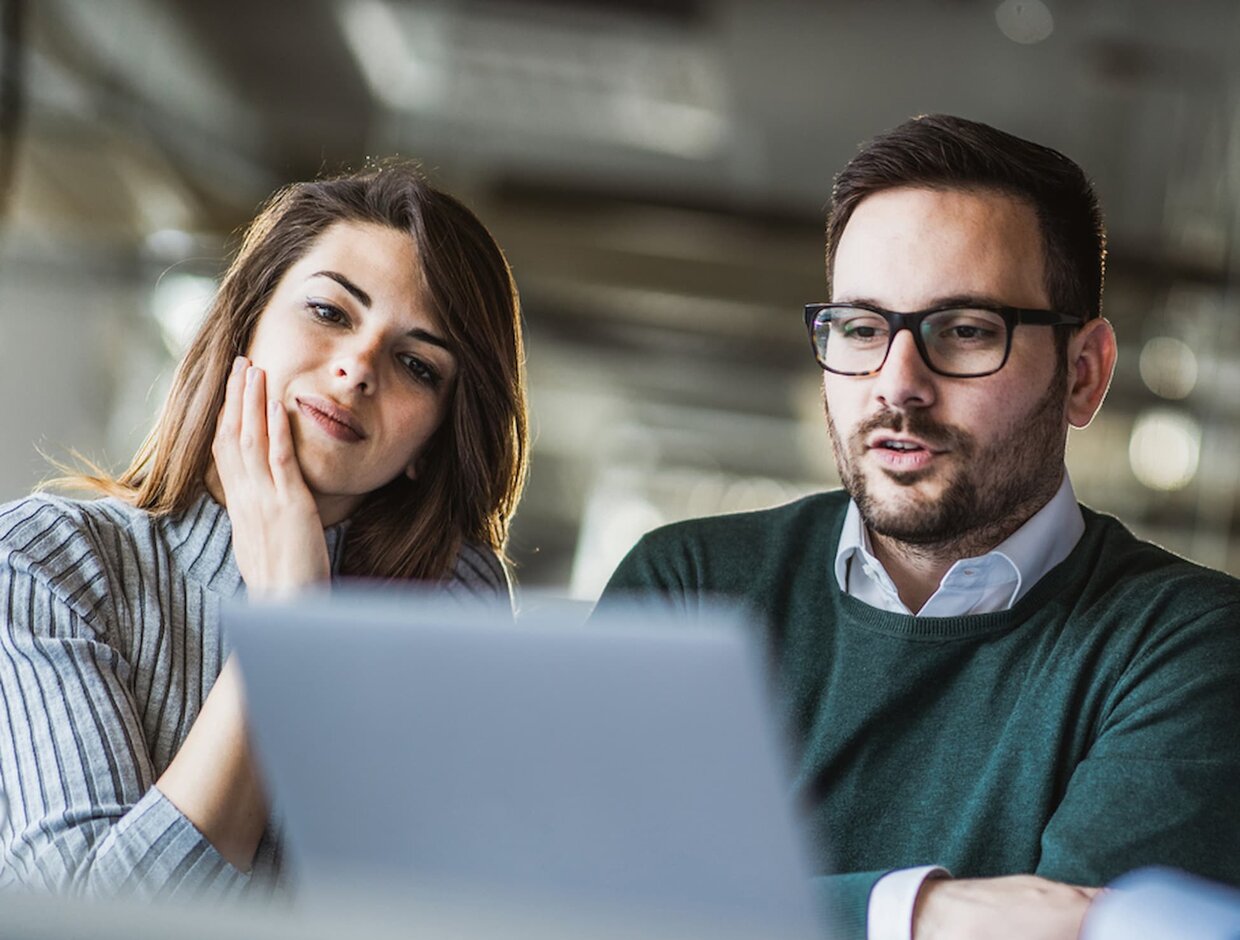 Meeting zwischen junger Frau und Mann mit Brille, die gemeinsam konzentriert auf einen Laptop-Bildschirm schauen.