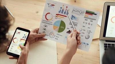 Investition dargestellt durch Personen, die bunte Geschäftsdiagramme auf Papier und Smartphone analysieren und besprechen.