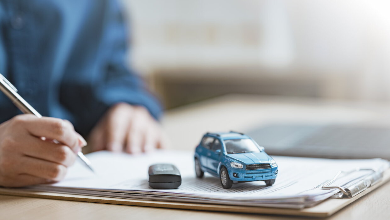 Eine Person unterschreibt ein Dokument, ein Modellauto Spielzeugauto auf dem Tisch.