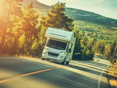 Wohnmobil über Mietkauf finanziert fährt auf der Straße durch hügelige Waldlandschaft